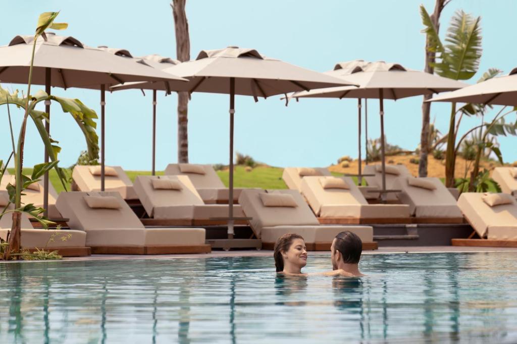 Pāris atpūšas baseinā pie LIU Resorts, zem saules aizsargiem.