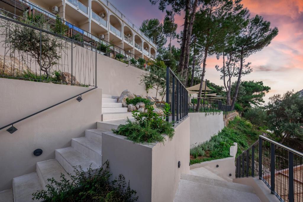 Skaista ainava ar trepēm, kas ved uz viesnīcu, ko ieskauj zaļumi un koki, ar mierīgu saulrietu debesīs.