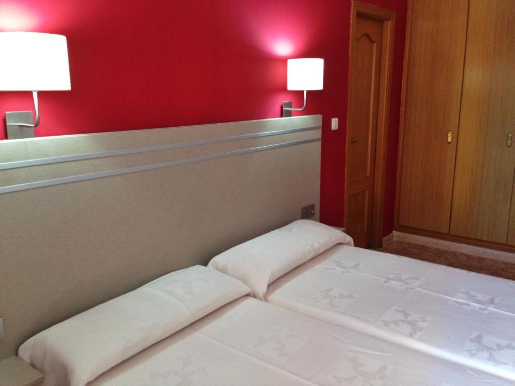 Guļamistaba ar divām gultām, sarkanu sienu un modernām gaismas ķermeņiem, kas rada siltu atmosfēru. Telpā ir koka skapji un mīksti gultas veļa.