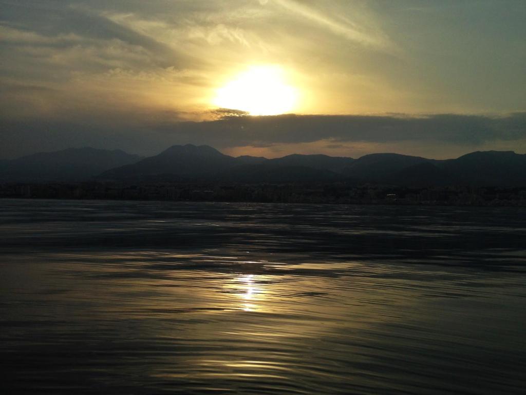 Saulriets virs kalniem, atspoguļojoties mierīgā ūdenī, rada skaistu un mierīgu ainavu. Debesīs redzamas smalkas mākoņu līnijas, kas piešķir ainavai papildu noskaņu.