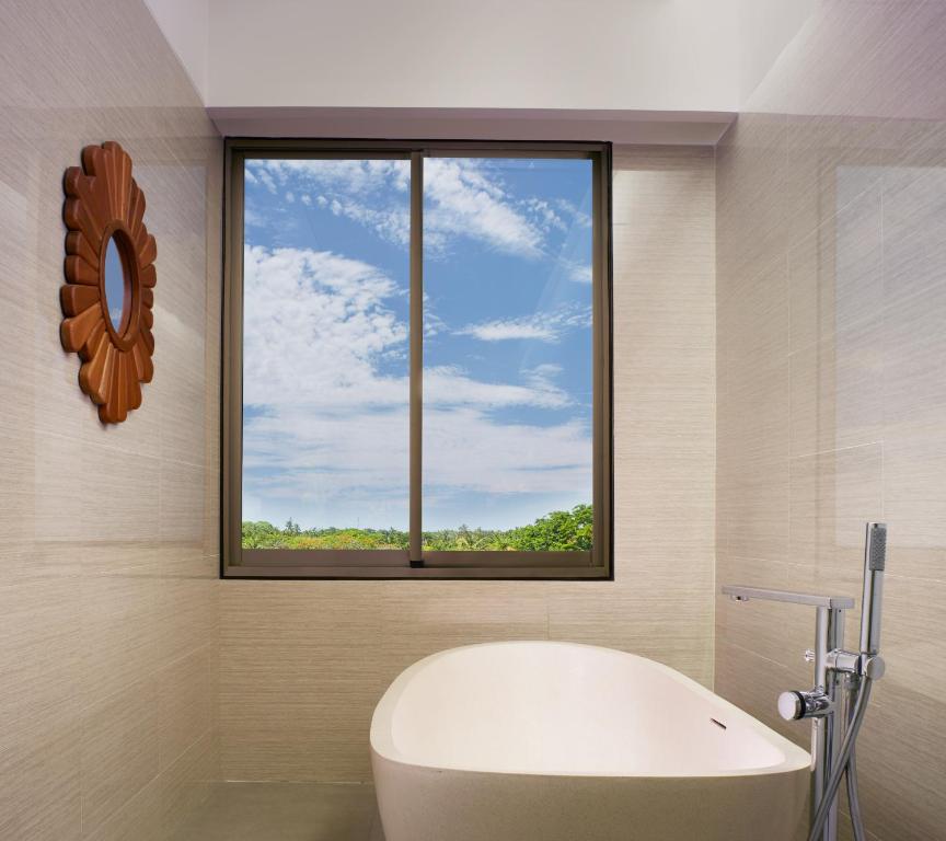 Mūsdienīga vannas istaba ar lielu vannu, koka spoguli un panorāmas logu, caur kuru redzama zaļa daba un zila debesis.