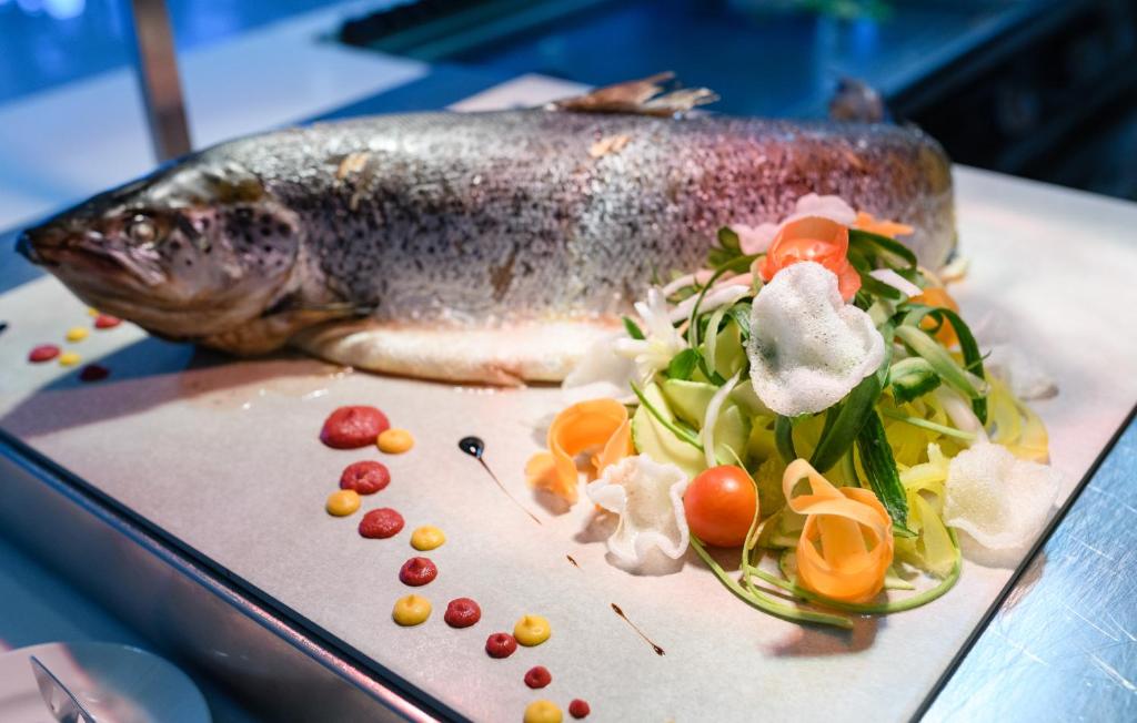 Svaiga zivs pasniegta ar krāsainiem dārzeņu salātiem un dekoratīvām mērcēm, radot pievilcīgu un gastronomiski izsmalcinātu ēdienu.