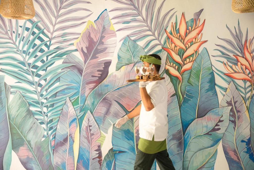 Apkalpotājs nes pasūtījumus pie Prime Plaza Hotel Sanur ar krāsainu fona gleznu.