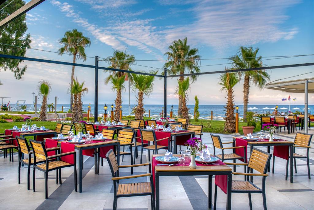 Āra restorāns pie jūras Sealife Kemer Resort Hotel, ar galdiem un palmām.