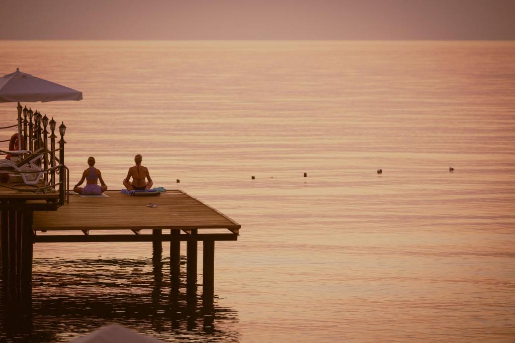 Divas sievietes meditē uz mola Sealife Kemer Resort Hotel piekrastē.