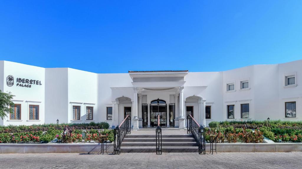 Iberotel Palace viesnīcas ieeja ar ziedu dārzu un skaidru debesu fonu.