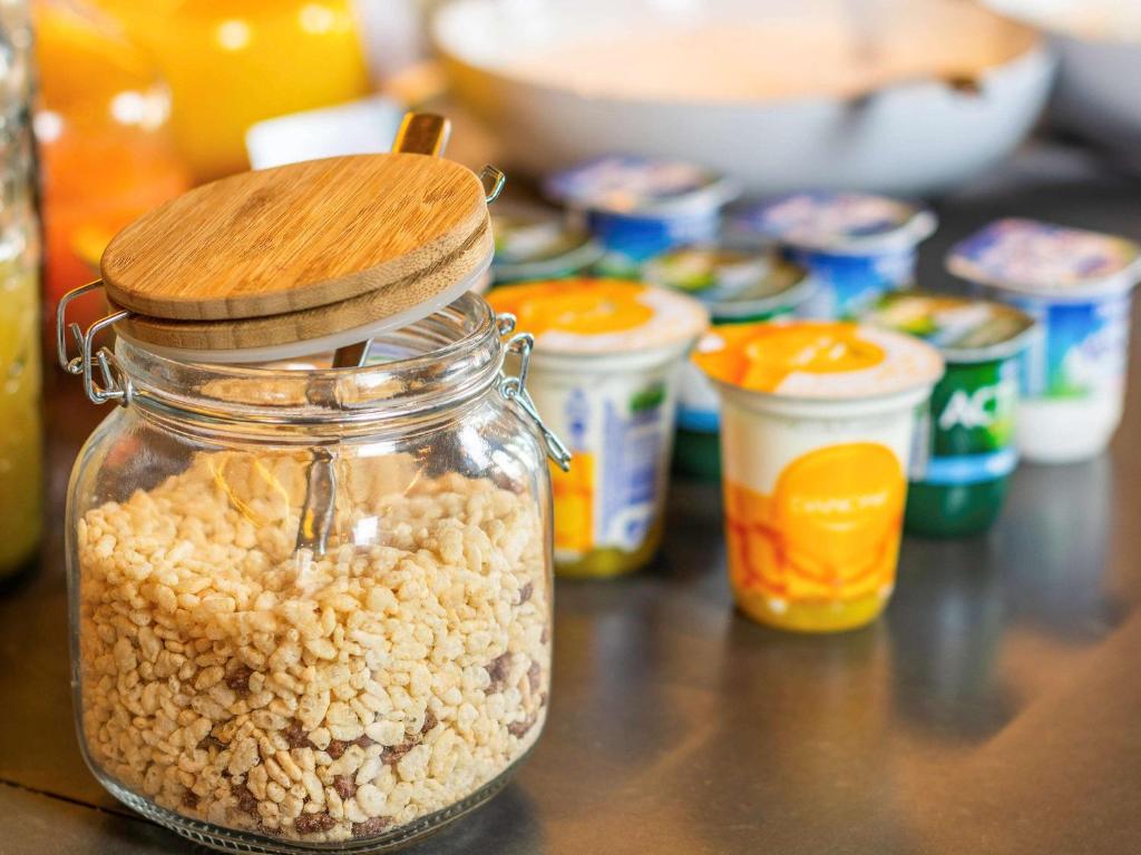 Stikla burkā ar koka vāku glabā rīsu pārslas, kam blakus ir dažādi jogurti un augļu dzērieni.