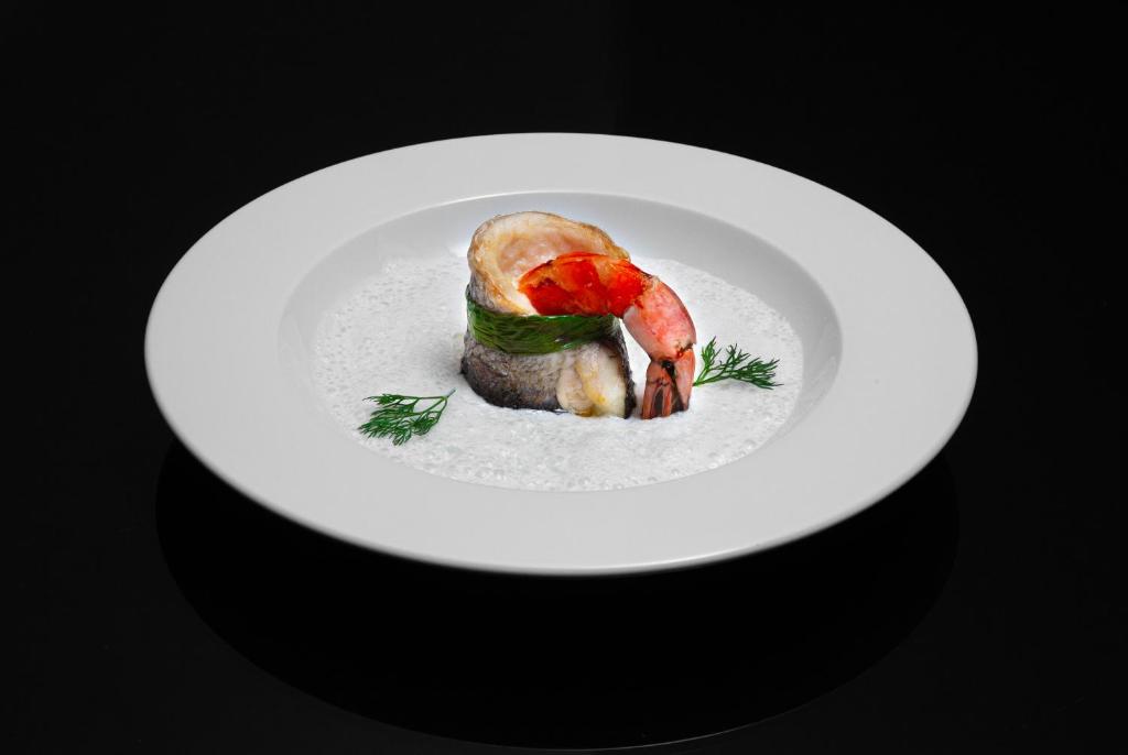 Eleganta jūras velšu porcija ar garnelēm, pasniegta uz baltas šķīvja ar krēmīgu mērci un zaļumiem.