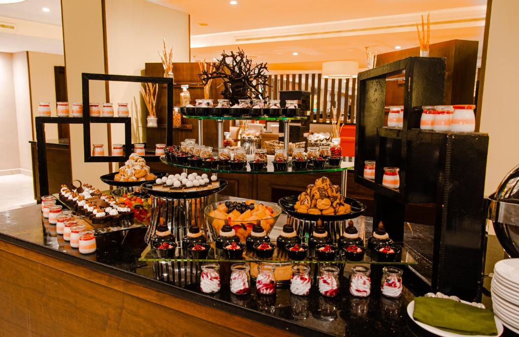 Dekorēts deserts galdiņš ar dažādiem saldumiem, tostarp kūkām, augļiem un krēmiem, pieejams viesnīcā. Saldumu izvēle ir plaša un vizuāli pievilcīga.