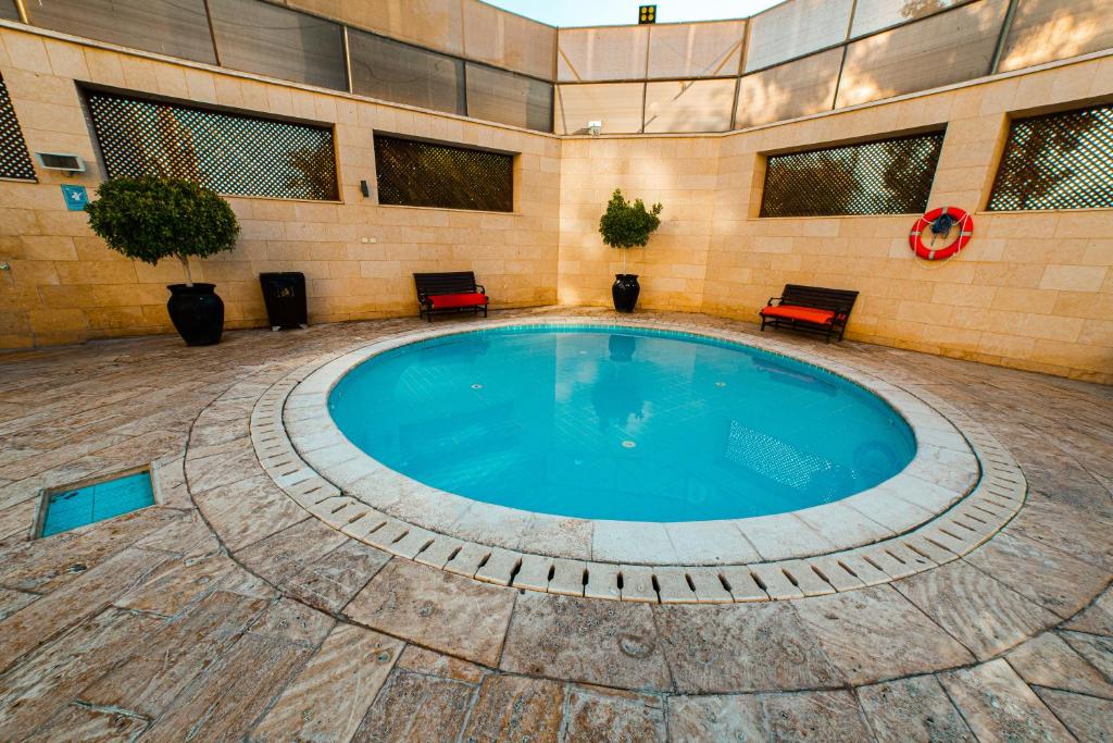 Moderns peldbaseins ar apaļu formu, ko ieskauj akmens sienas un dārza elementi. Apkārt baseinam ir sarkanas krēsli un glābšanas riņķis.