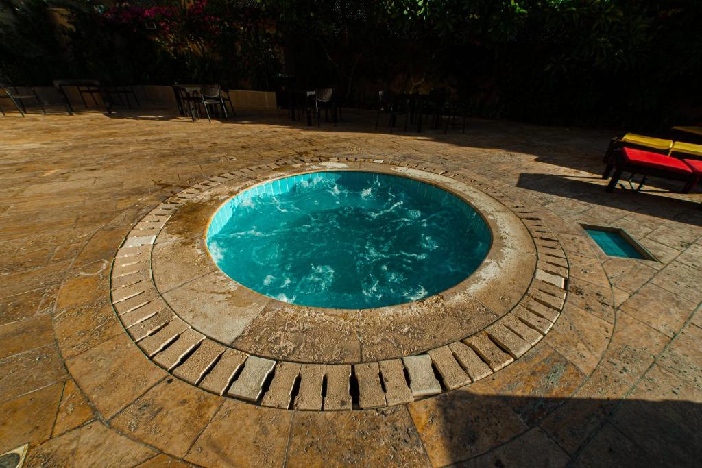 Apsildāms baseins ar dzidru ūdeni, ieskauts ar akmens flīzēm un zaļām augiem. Apkārt baseinam ir sēdvietas un galds, kas rada relaksējošu atmosfēru.