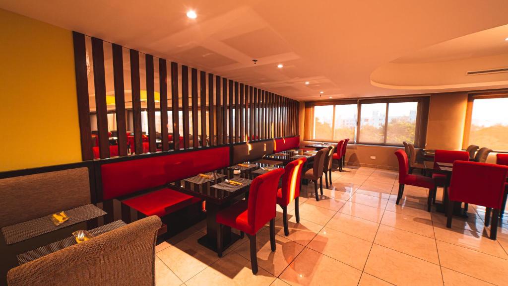 Mūsdienīga restorāna interjers ar sarkaniem un pelēkiem krēsliem, elegantām galdiem un lieliem logiem, kas nodrošina dabiski apgaismojumu.