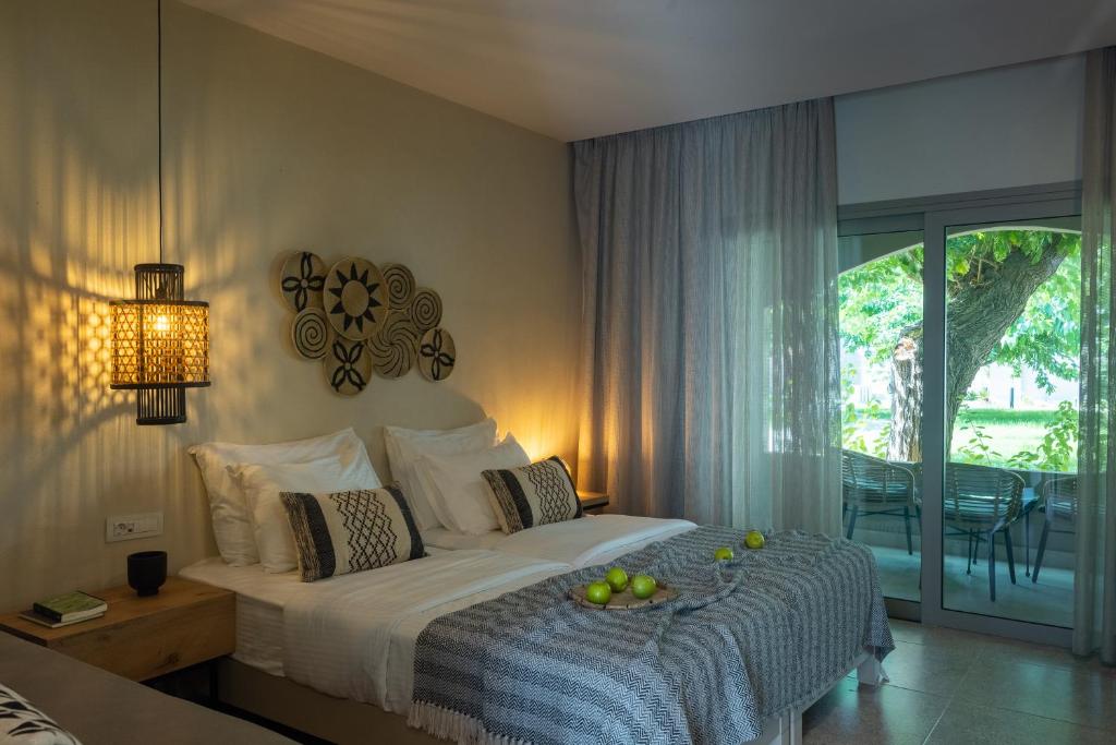 Mūsdienīgs guļamistabas interjers ar divguļamo gultu, stilīgu apgaismojumu un skatu uz dārzu. Telpā ir arī dabīgas krāsas un dekoratīvi elementi, kas rada mierīgu atmosfēru.