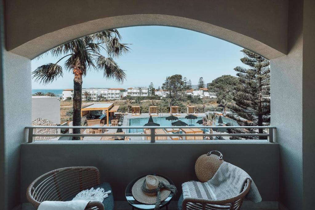 Skats no balkona uz pludmales viesnīcu ar palmām un peldbaseinu. Eleganta atpūtas zona ar vīna glāzi un segu.