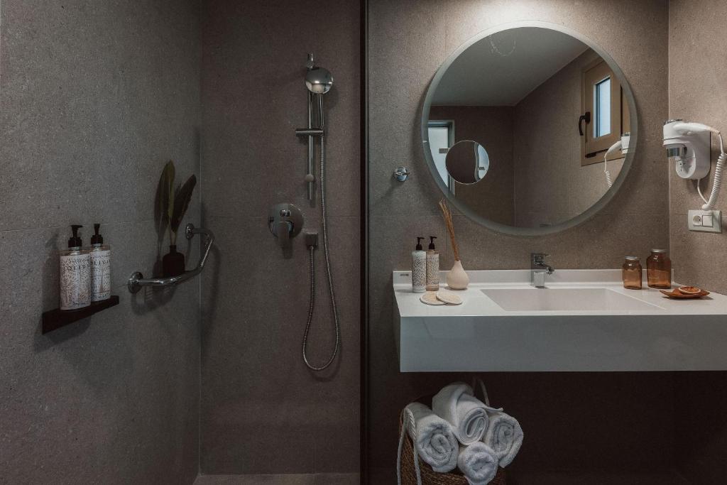 Mūsdienīgs vannas istabas interjers ar dušu, apaļu spoguli un stilizētu izkārtojumu. Uz plauktiņa ir dažādas ķermeņa kopšanas līdzekļu pudeles un dekoratīvi elementi.