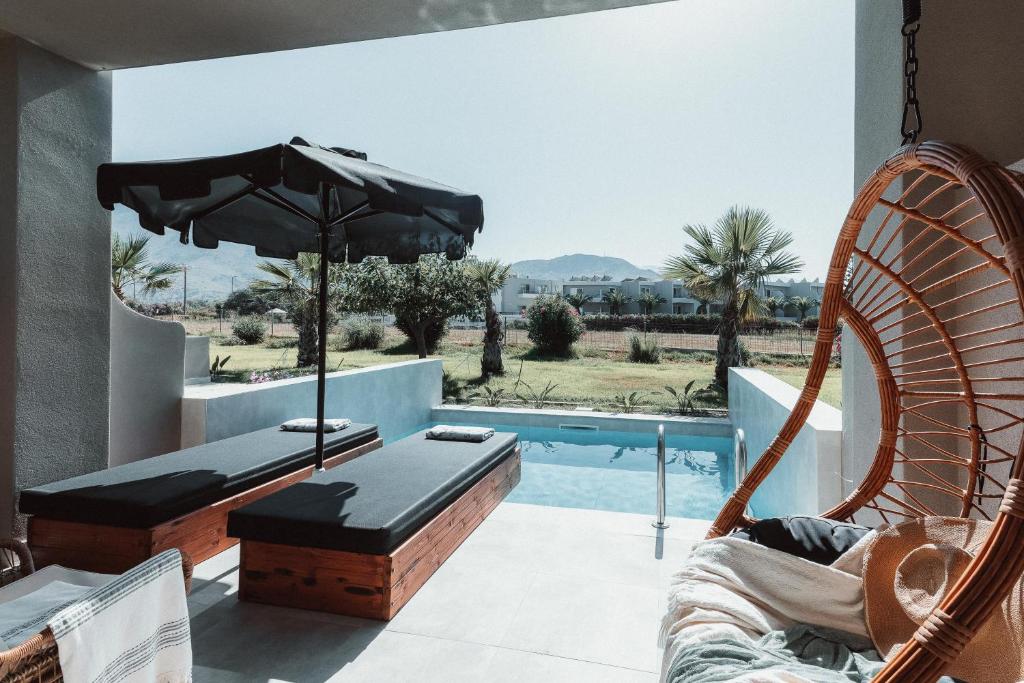 Mūsdienīgs atpūtas stūrītis ar baseinu, sauļošanās krēsliem un ēnainu saulessargu. Fonā redzamas palmas un kalnu ainava.