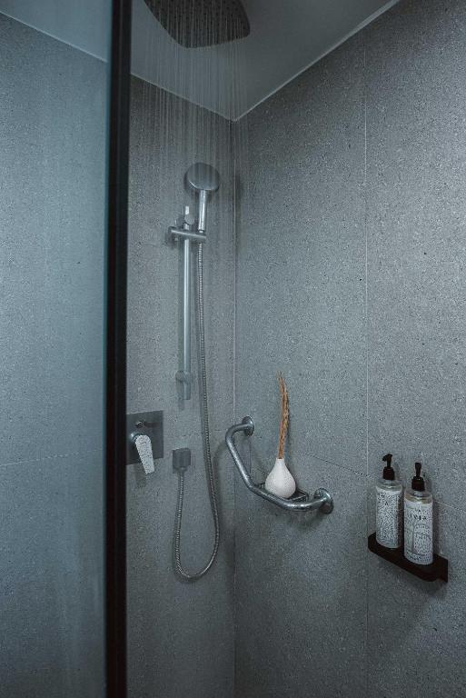 Mūsdienīga duša ar pelēkām flīzēm, hromētu dušas jaucējkrānu un stilīgām higiēnas līdzekļu pudelēm. Interjers ir elegants un minimālistisks.