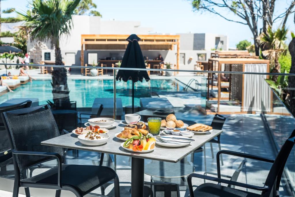 Broka ar gardu brokastu klātbūtni pie baseina, kurā redzami augļi, maizes izstrādājumi un dzērieni, radot relaksējošu un viesmīlīgu atmosfēru.