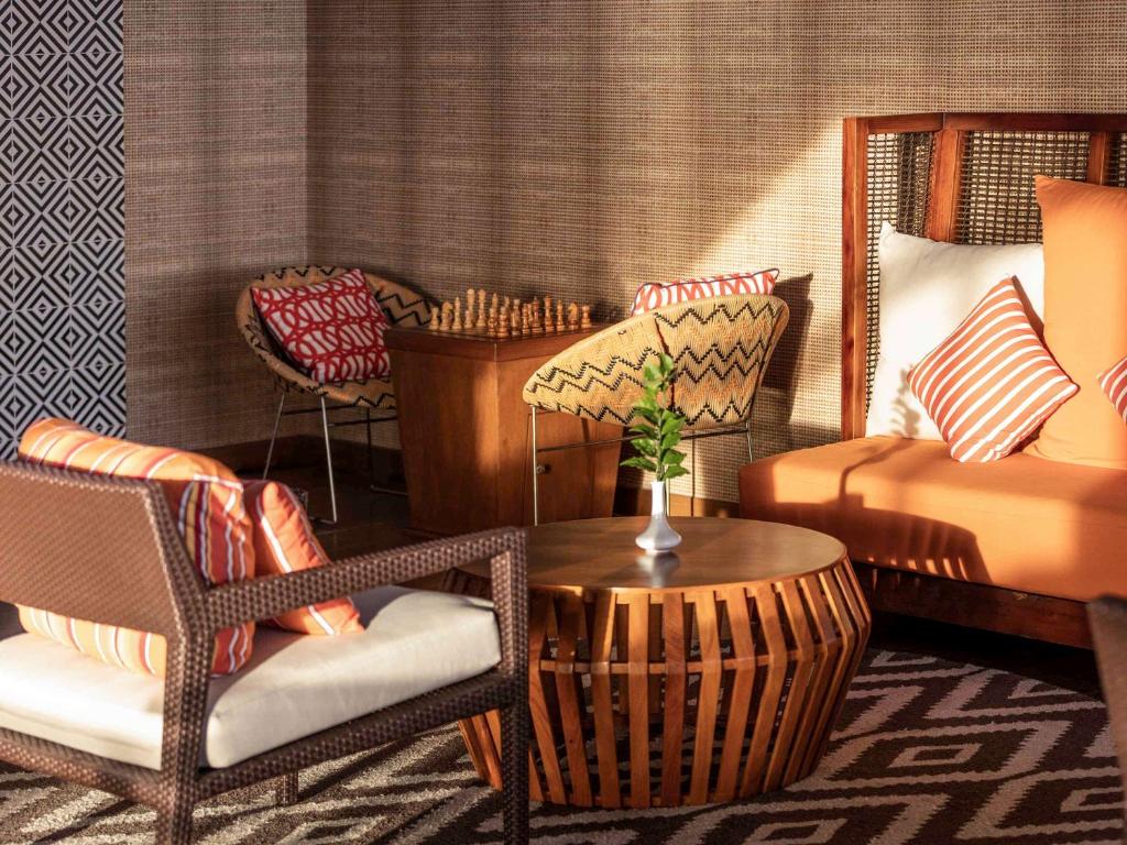 Mūsdienīgs viesnīcas interjers ar komfortablu sēdvietu zonu, kas ietver krēslus un dīvānu ar spilveniem, kā arī koka galdiņu un šaha spēli. Eleganta apdare un siltas krāsas rada patīkamu atmosfēru.