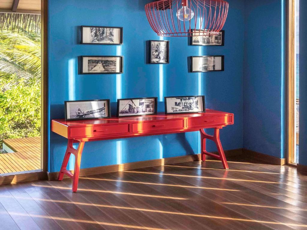 Sarkans konsoles galds ar melnbaltām fotogrāfijām uz zila fona, apgaismotas ar dabiskiem gaismas stariem. Interjers izceļ mūsdienīgu un krāsainu dizainu.