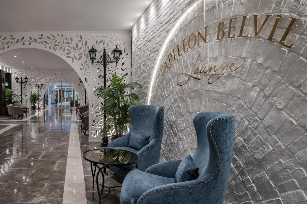 Viesnīcas Papillon Belvil elegantā atpūtas zone ar zilo krēslu un dekoratīvu sienu.