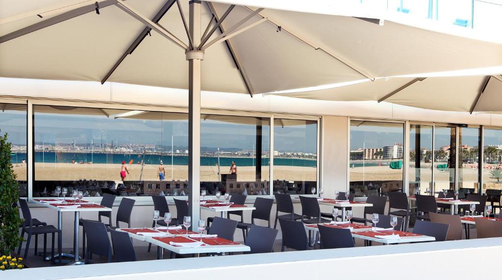 Restorāna terase ar skatu uz pludmali un jūru, kurās ir galdi ar galda piederumiem un saulessargi. Ideāla vieta atpūtai un maltītēm pie ūdens.