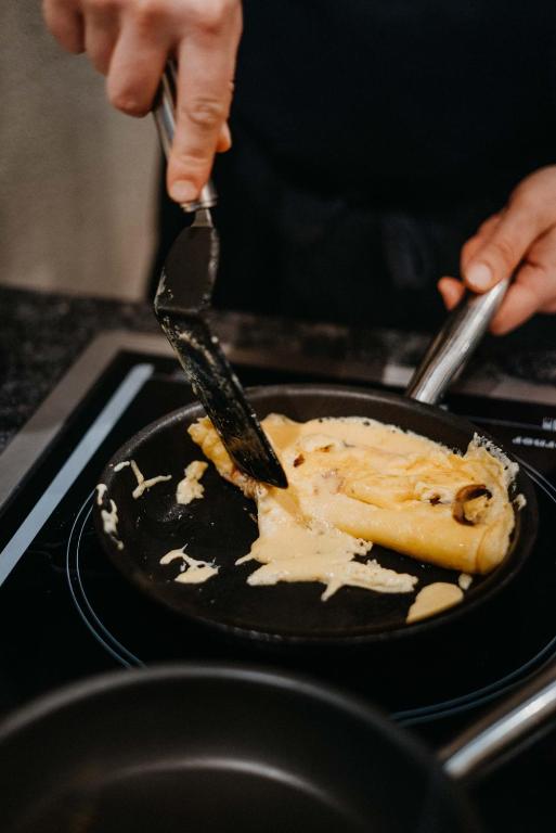 Kulinārā skatuve, kurā kāds pagatavo omleti pannā, izmantojot lāpstiņu. Pannā redzami olu maisījumi un sēnes.