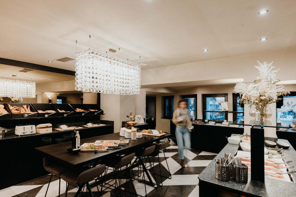 Eleganta brokastu zona ar modernu interjeru, kurā redzami bagātīgi pārtikas galdi un stilīgas gaismas. Pievilcīgā vide ir ideāla relaksācijai un maltītēm.