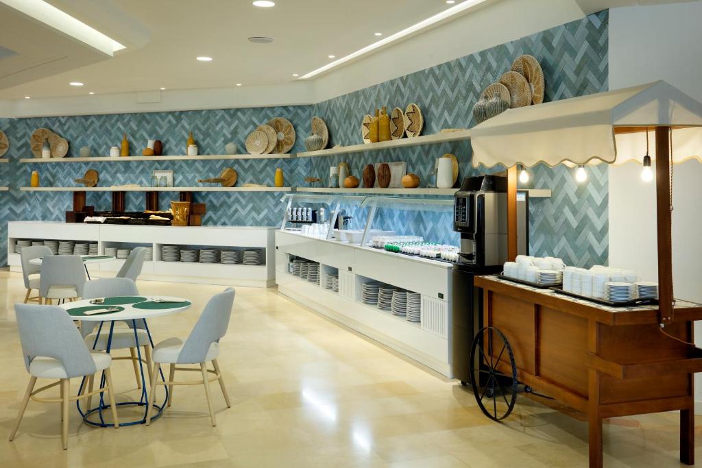 Mūsdienīga kafijas telpa ar gaišu interjeru, kurā redzami eleganti galdi un krēsli, kā arī stilīgi plaukti ar dekoratīviem priekšmetiem un traukiem.