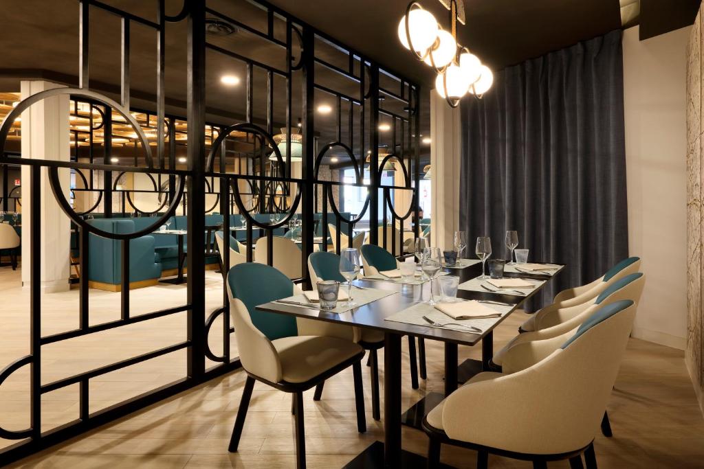 Moderns restorāns ar elegantu interjeru, kas iekārtots ar stilīgām krēsliem un galdiem, radot patīkamu atmosfēru. Redzams arī dekoratīvs elements un aizkaru fons.