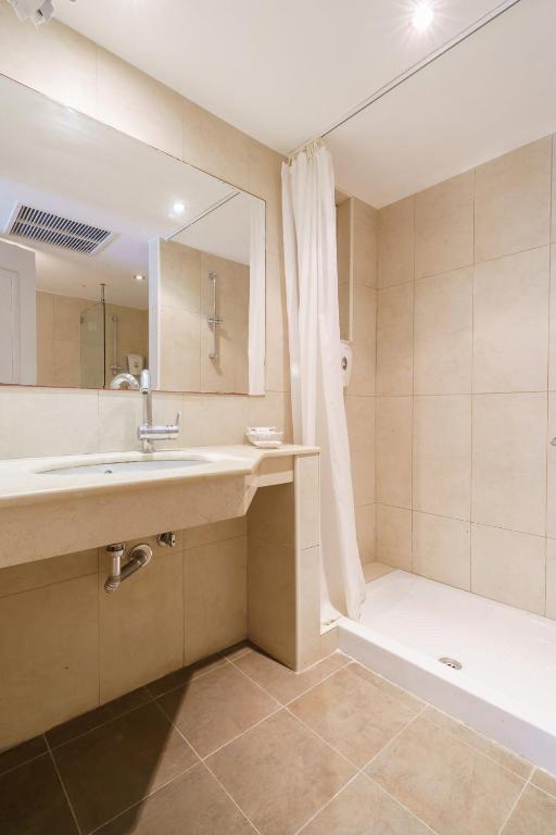 Moderns vannas istabas interjers ar gaišām flīzēm, plašu spoguli un dušas zonu ar aizkaru. Eleganta un funkcionāla dizaina elementi, kas nodrošina komfortu.