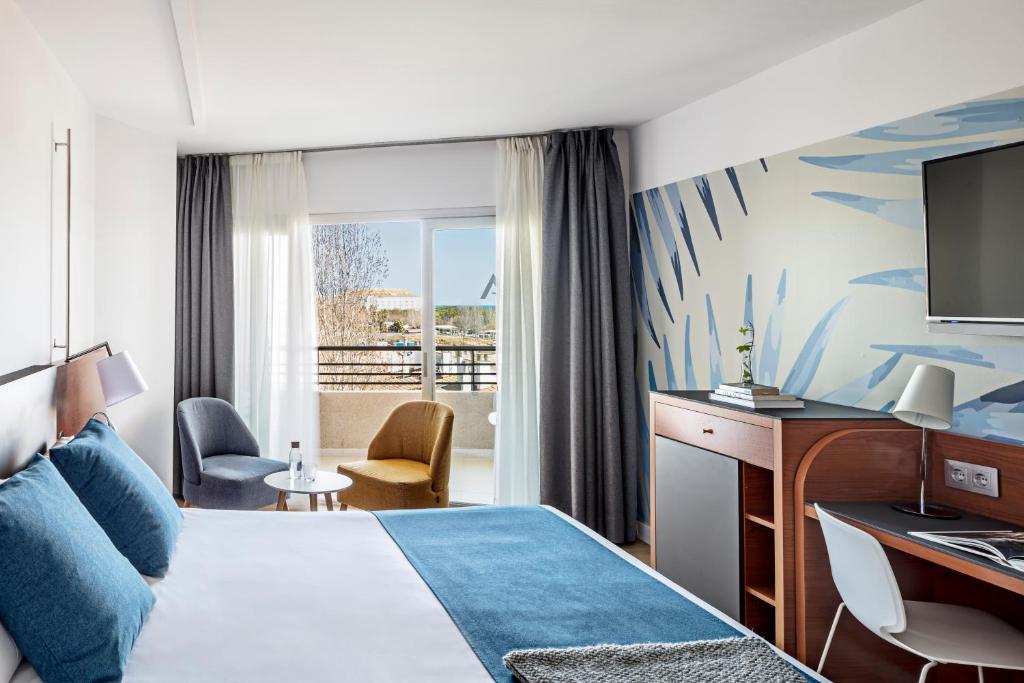 Mūsdienīga viesnīcas numura iekārtojums ar jūras skatu, gaišām krāsām un ērtiem mēbeļu elementiem, piemēram, krēsliem un galdu. Numurā ir liela gulta un televizors.