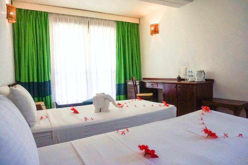 Komfortabls numurs viesnīcā Club Bentota ar divām gultām un zaļiem aizkariem.