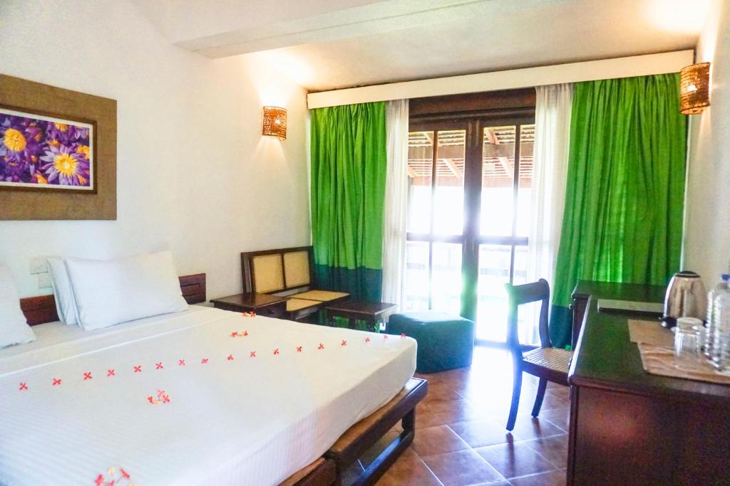 Club Bentota viesnīcas numurs ar dabisku apgaismojumu un zaļiem aizkariem.