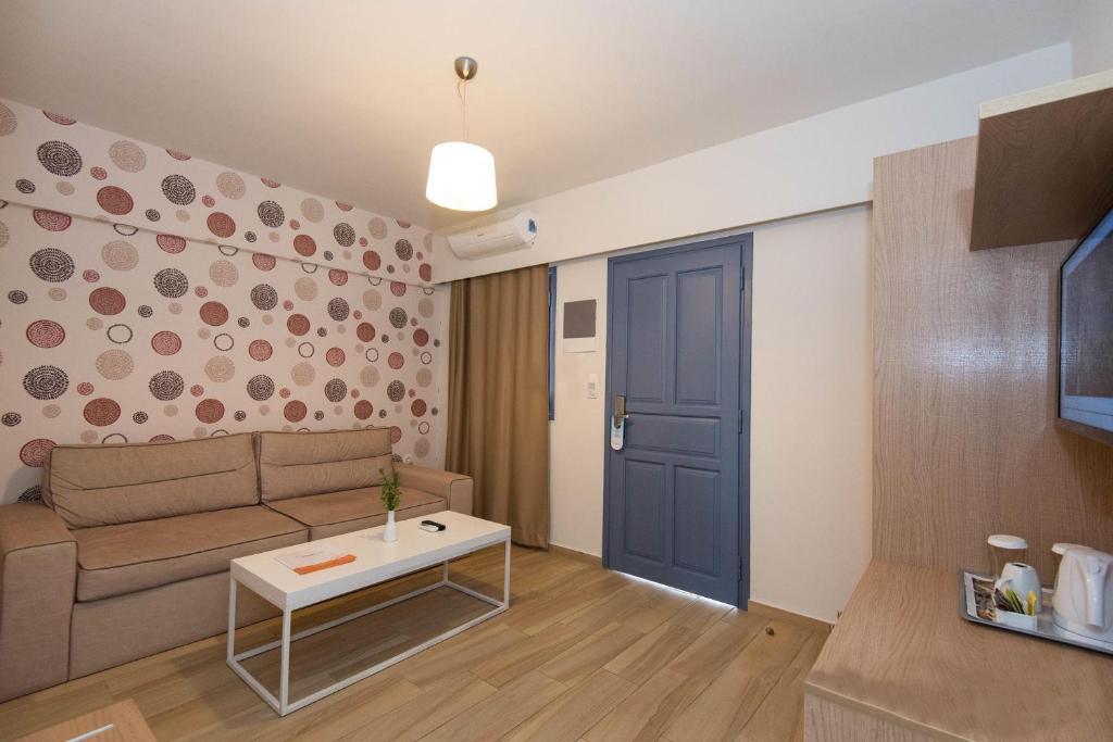 Mūsdienīga viesistaba ar gaišiem toņiem, mīksto dīvānu un rakstainām tapetēm. Telpā redzams galds ar ziedu un virtuvītes stūris.