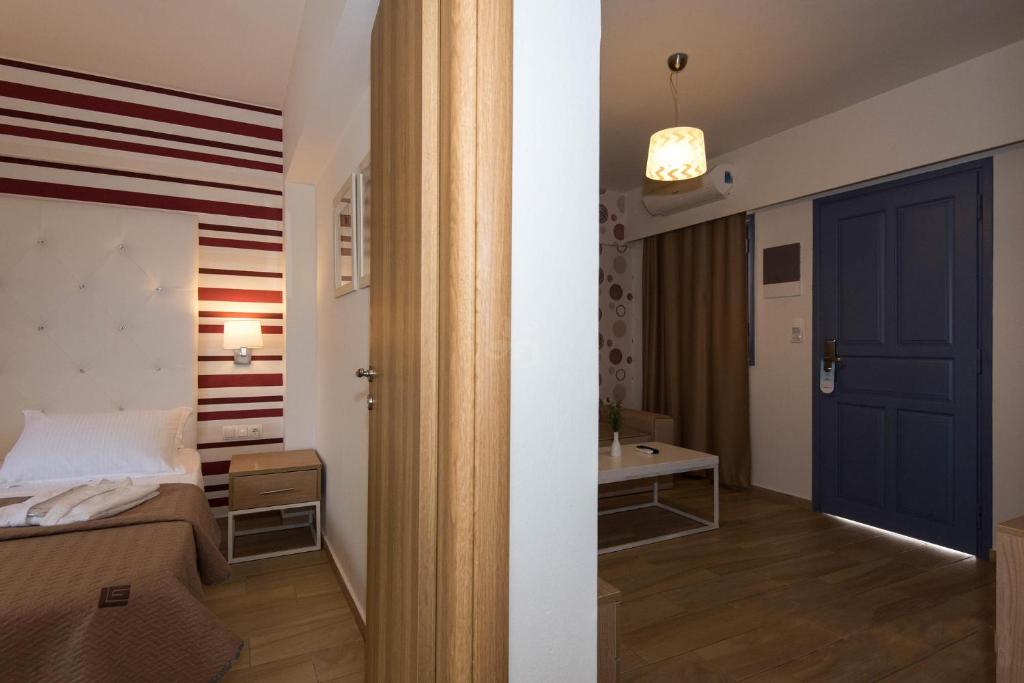 Mūsdienīga viesnīcas istaba ar elegantu interjeru, kas ietver gultu ar baltiem un brūniem akcentiem, kā arī viesistabu ar dīvānu un galdu. Durvis ved uz ārpusi, radot viesmīlīgu atmosfēru.