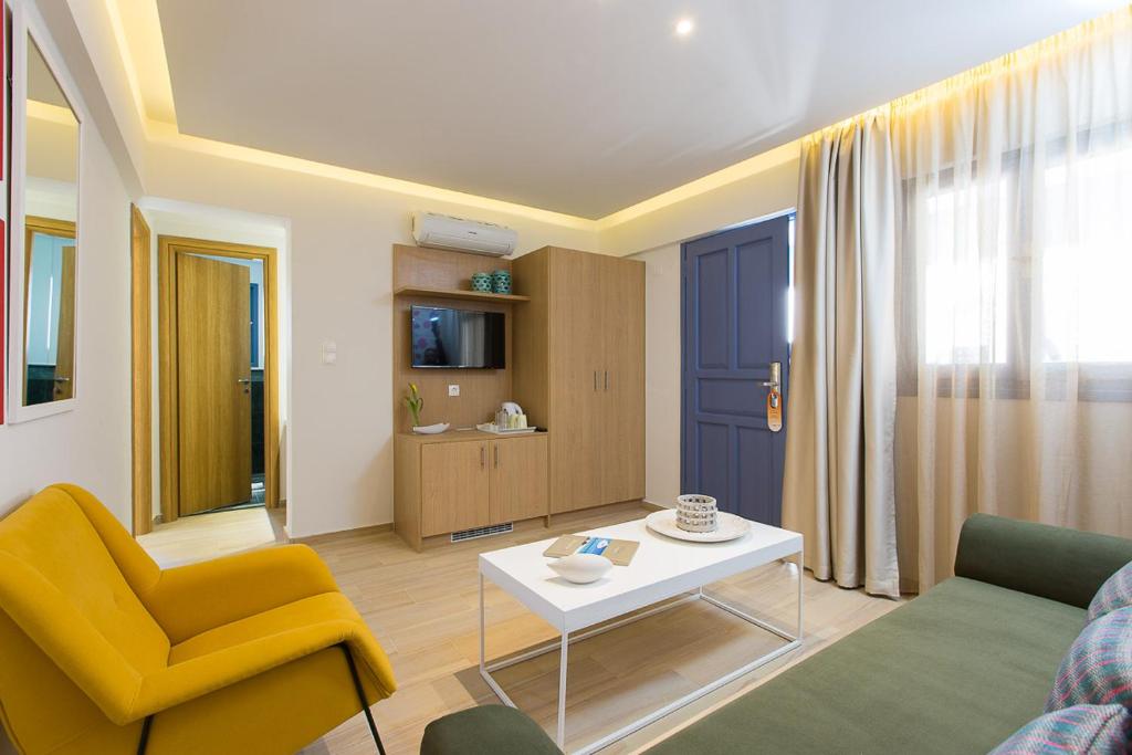 Mūsdienīgs viesistabas interjers ar dzeltenu krēslu, zaļu dīvānu un skaidriem logiem, kas nodrošina dabīgu apgaismojumu. Telpā ir televizors, koka mēbeles un gaiši toņi, radot siltu un mājīgu atmosfēru.