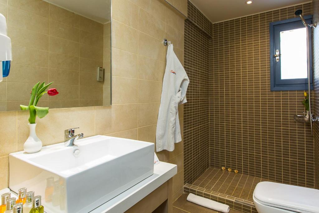 Moderns vannas istabas interjers ar gaišām flīzēm, plašu izlietni un dušas stūri. Vāzē ir zieds, kas piešķir telpai dzīvīgumu.