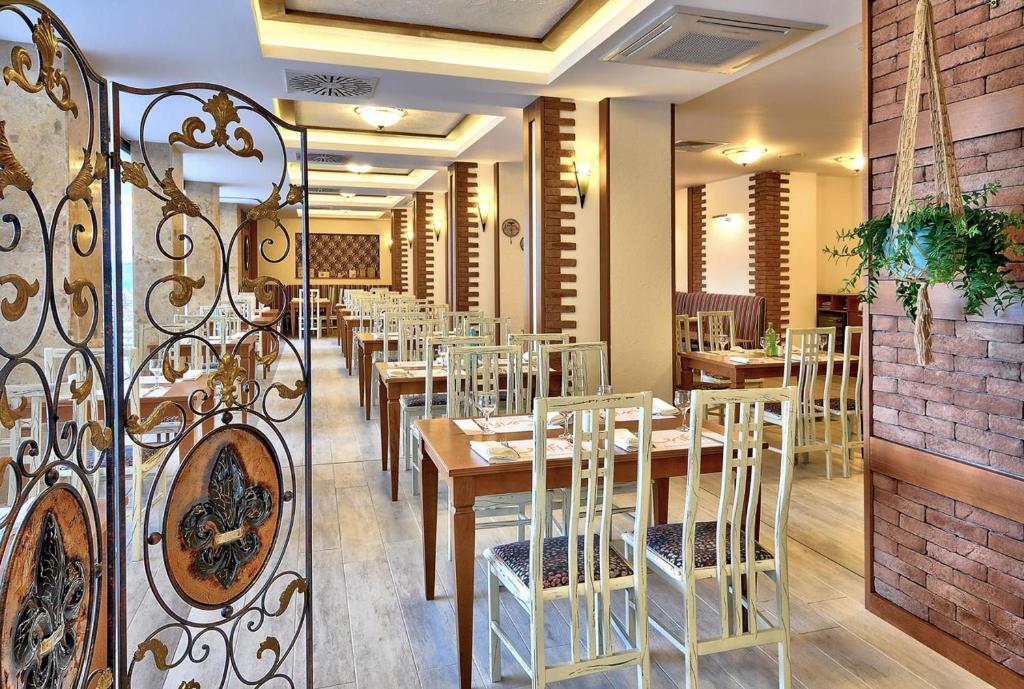 Elegantā restorāna interjers ar koka galdiem un krēsliem, dekoratīvām detaļām un augu kompozīcijām. Gaisotne ir silta un viesmīlīga, ideāla maltīšu baudīšanai.