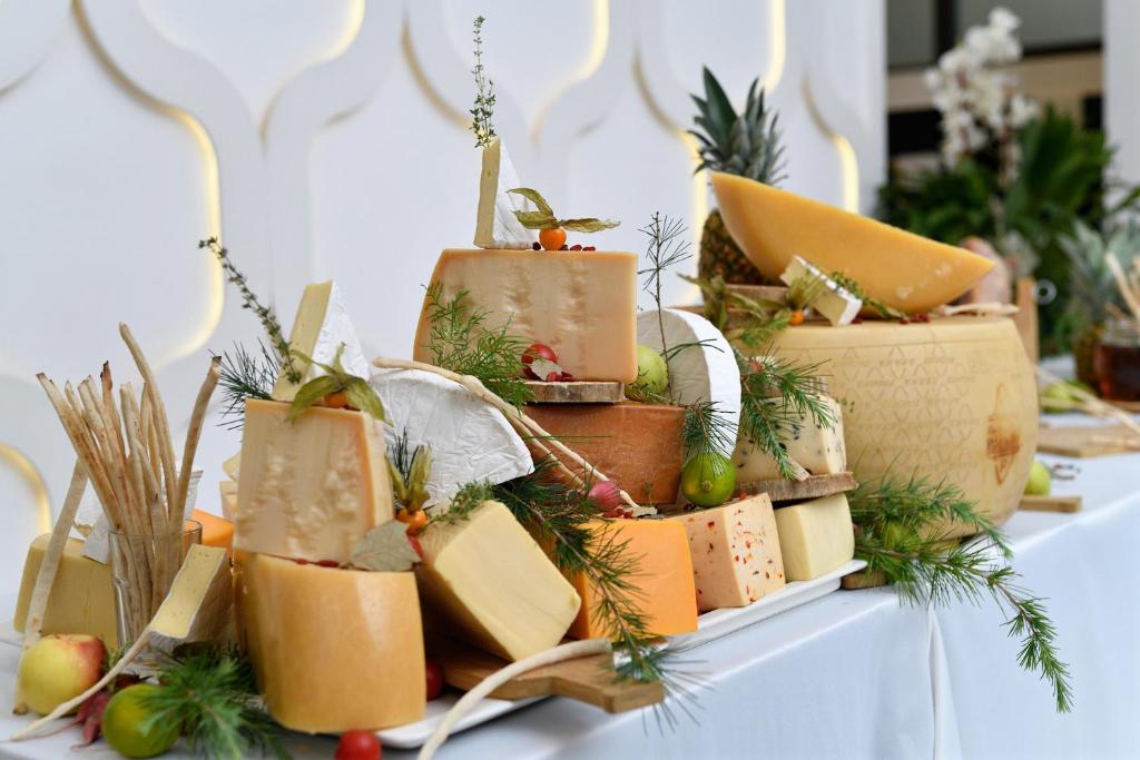 Siera izkārtojums ar dažādām siera šķirnēm, rotāts ar zaļumiem un augļiem, radot elegantu un gaumīgu pasākuma uzkodu galdu.
