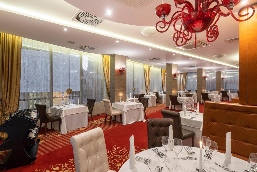 Elegants restorāns ar stilīgu interjeru, kurā ir balti galdauti un sarkanā paklāja. Dabbās lustras un mīkstas krēslus nodrošina patīkamu atmosfēru.