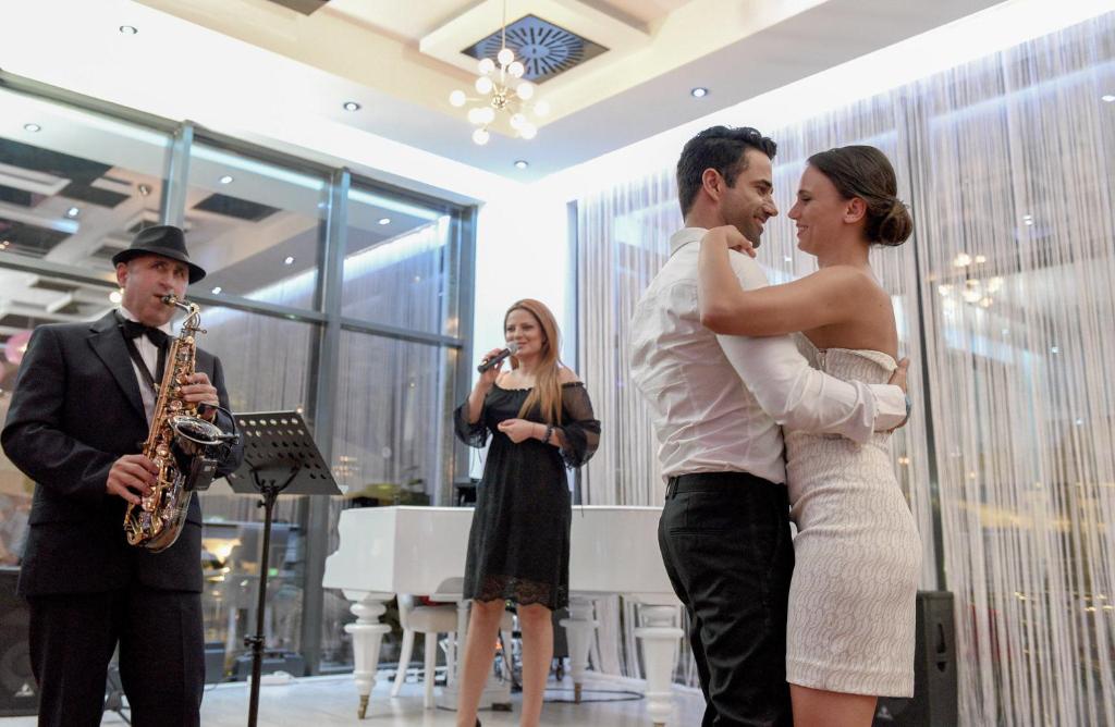 Romantisks mirklis, kur pāris dejo, kamēr mūziķis spēlē saksofonu un dziedātāja uzstājas. Eleganta atmosfēra modernā izklaides vietā.