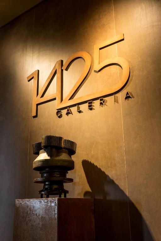 1425. gada galerijas logo ir redzams uz sienas, blakus stilizētiem mehāniskiem elementiem, radot mūsdienīgu un māksliniecisku atmosfēru.
