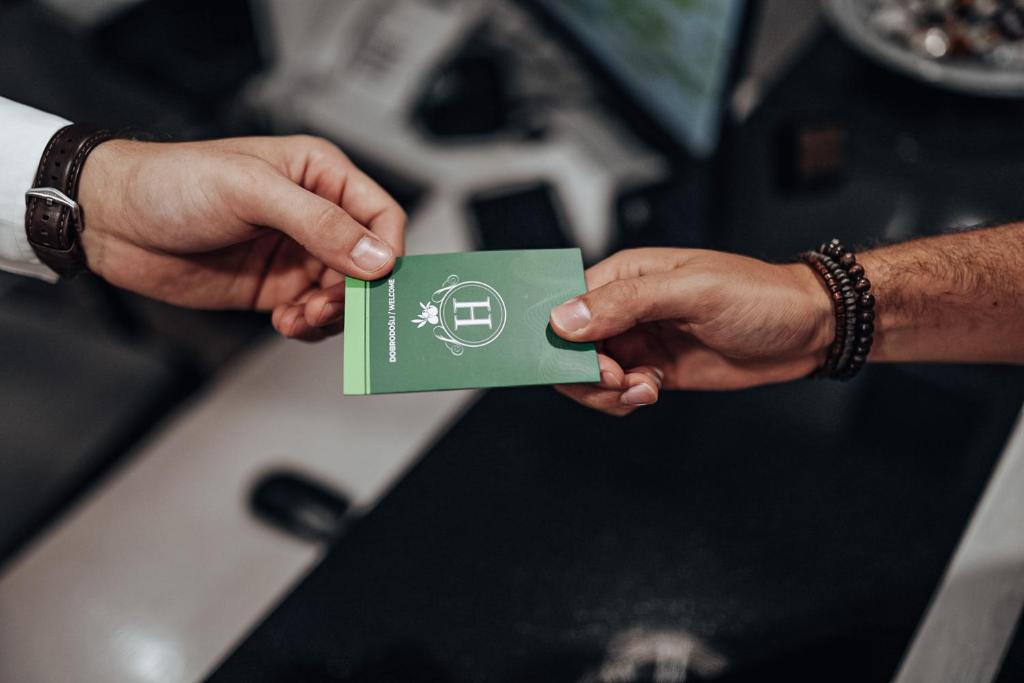 Zaļas kartes nodošana, kas varētu būt viesnīcas vai pakalpojumu karte, starp divām rokām pie reģistratūras galda.