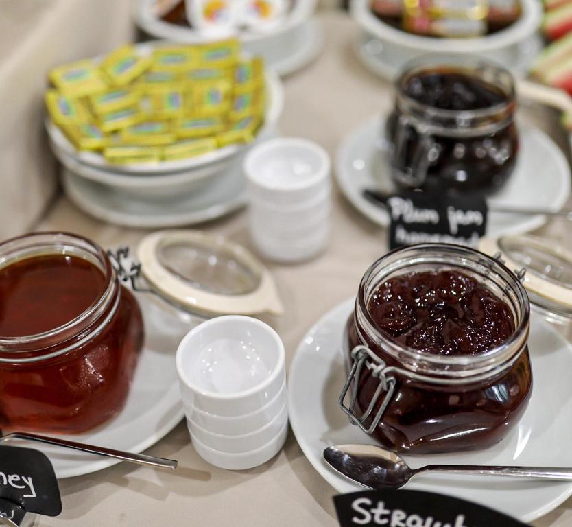 Dažādas ievārījumu un medus burkas, kas novietotas uz galda kopā ar maziem traukiem un karotēm. Ideāli piemērots brokastīm vai uzkodām.