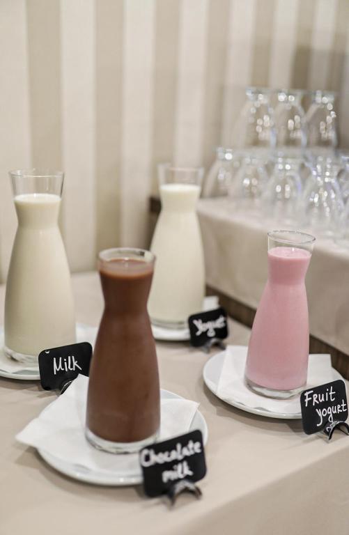 Svaigu dzērienu stends ar pienu, šokolādes pienu, jogurtu un augļu jogurtu, katrs pasniegts caurspīdīgā glāzē ar nosaukumu uz melna zīmuļa.