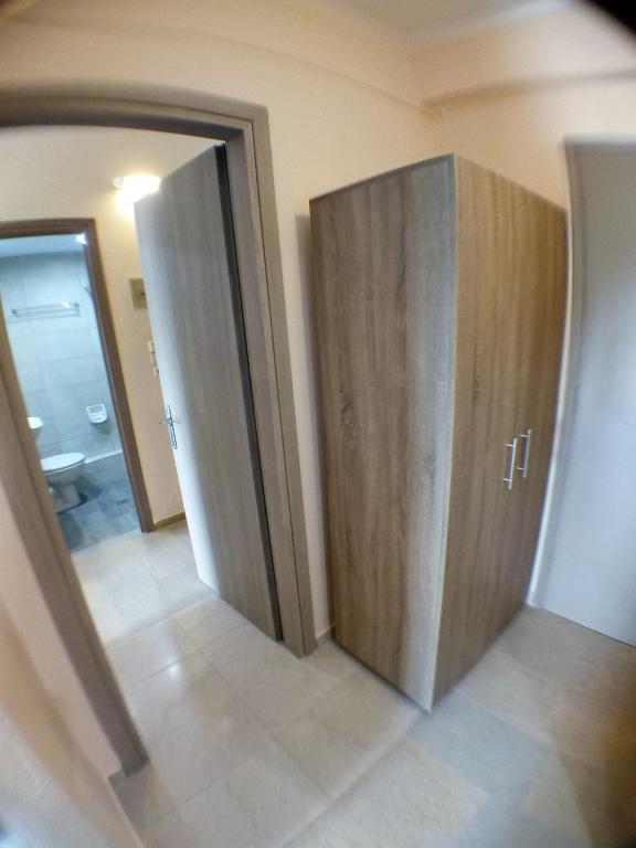 Mūsdienīgs gaitenis ar koka skapjiem, kas nodrošina uzglabāšanas iespējas. Redzama piekļuve vannas istabai ar pelēku flīžu grīdu.
