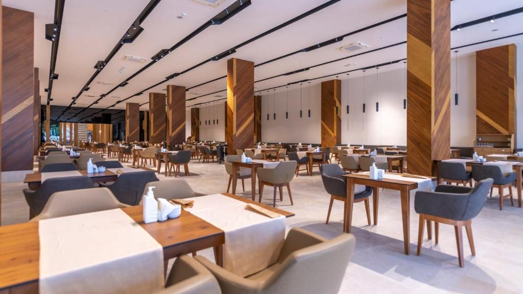 Moderns restorāns ar elegantiem koka galdiem un krēsliem, plaša telpa ar dabiskiem apgaismojumiem un dekoratīvām koka kolonnām. Ideāla vieta gastronomiskām pieredzēm.