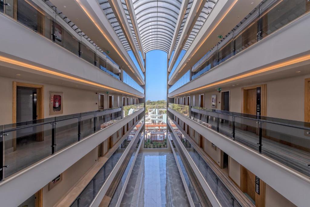 Mūsdienīgs viesnīcas interjers ar plašu skatu uz apgaismotu koridoru un zilu debesi. Apgaismojums un stikla balkoni rada elegantu atmosfēru.