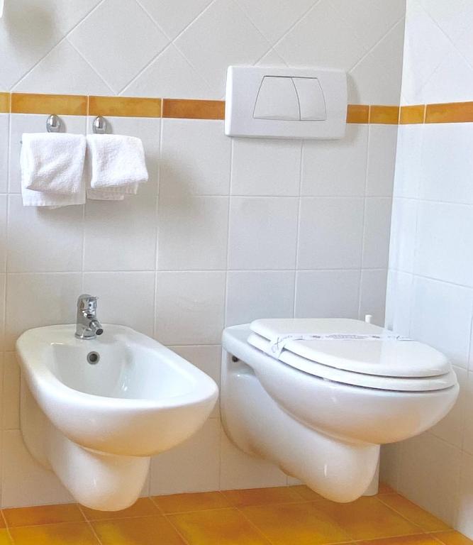 Baltas tualetes un bidē ierīces modernā vannas istabā, ar divām dvieļu turētājiem uz sienas.